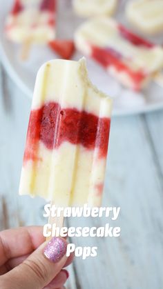 a hand holding a popsicle with red and white toppings on it, in front of a plate of strawberries