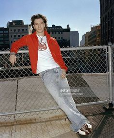 a young man leaning against a fence in the city