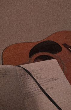 an open book with a guitar in the background and a pen resting on top of it