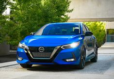 a blue nissan vehicle parked in front of a building with trees and bushes behind it