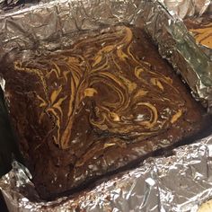 a piece of chocolate cake sitting on top of tin foil covered in brown and yellow swirled icing