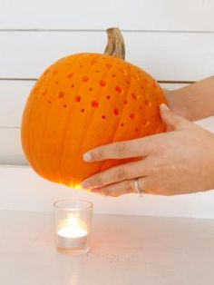 a person holding an orange pumpkin next to a candle