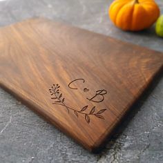 a wooden cutting board with the initials and date engraved on it next to two pumpkins