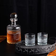 two glasses and a decanter are sitting on a table with a black background