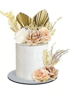 a white cake topped with flowers and gold leaves on top of a silver platter