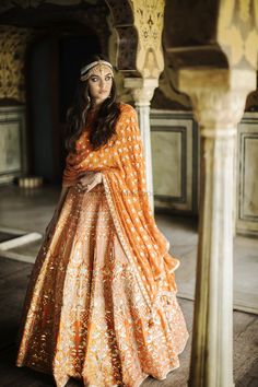 a woman in an orange and gold bridal gown posing for the camera with her hands on her hips