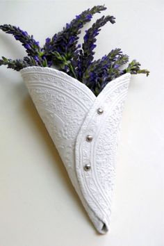 a white vase filled with purple flowers sitting on top of a table next to a wall