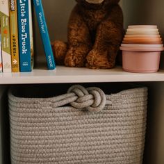 a stuffed bear sitting on top of a book shelf next to a basket and books