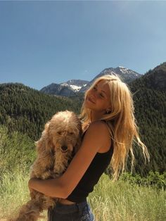 a woman is holding a dog in the mountains