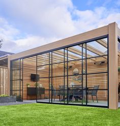 a glass enclosed patio with wooden walls and green grass in the foreground is an outdoor dining area