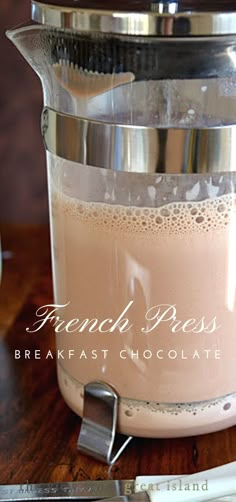 french press coffee maker with milk in it on a wooden table next to utensils