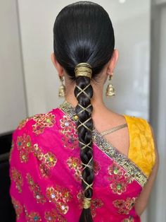 a woman with long black hair in a pink sari and gold jewelry is seen from the back