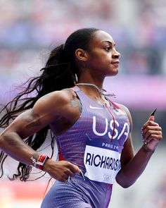 a woman running on a track with her hair blowing in the wind and tattoos on her arm