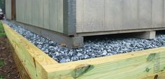 a wooden box sitting on top of gravel next to a green planter filled with rocks