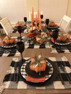 a dining room table set with black and white place settings, pumpkins on the plates