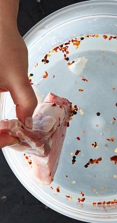 a person holding a piece of meat in front of a white bowl filled with food