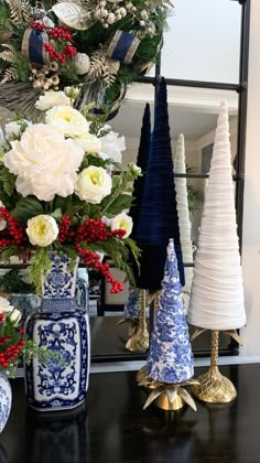 a christmas tree decorated with white and blue flowers in front of other holiday decorations on a black table