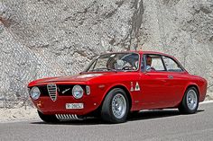 an old red car is parked in front of a large rock wall and there is no image on it