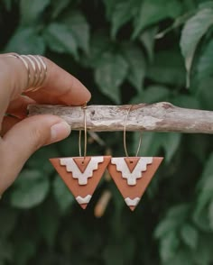 a pair of wooden earrings with geometric shapes hanging from the end of a tree branch