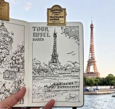 a hand holding up an open book with the eiffel tower in the background