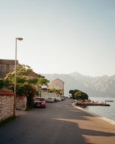 cars parked on the side of a road next to a body of water with mountains in the background