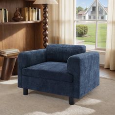 a blue chair sitting in front of a window next to a book shelf filled with books