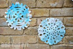 two paper snowflakes are hanging on a brick wall, one is blue and the other is white