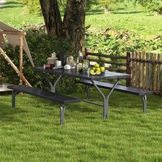 a picnic table with two benches in the grass near a tree and some fruit on it