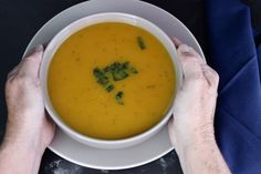 two hands holding a bowl of soup with broccoli