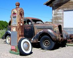 an old rusty gas pump sitting in the middle of a gravel lot next to a building