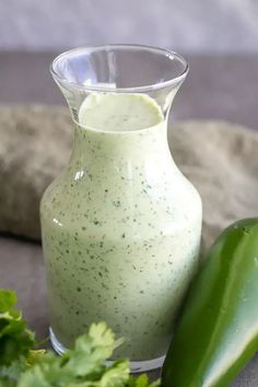 a cucumber is next to a small glass vase filled with green liquid on a table