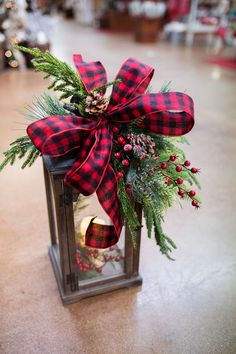 a christmas lantern with a red and black plaid bow on it, sitting on the floor