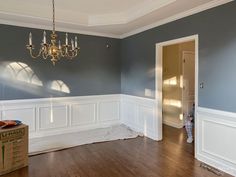 an empty room with hard wood floors and blue walls, chandelier hanging from the ceiling