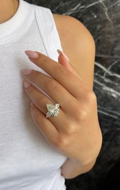 a woman's hand with a diamond ring on her left hand and a white tank top