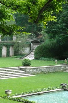 an outdoor garden with steps leading up to the water and trees in the background, surrounded by lush green grass