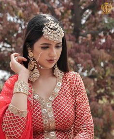 a woman in a red and gold outfit is holding her hands to her ear while looking down