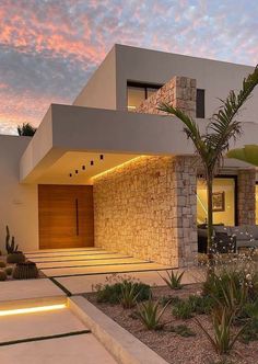 a modern house is lit up at night with lights on the windows and palm trees in front