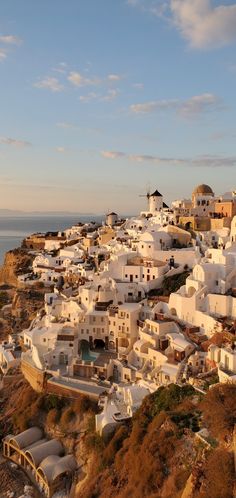 the white buildings are on top of the hill by the ocean and blue sky with clouds