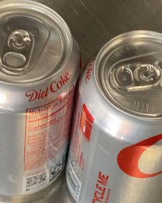 two cans of diet coke sitting next to each other on top of a metal table