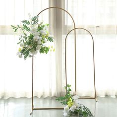 two gold stands with white flowers and greenery on them in front of a window