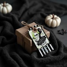 a brown box with a tag on it sitting on a black blanket next to small white pumpkins