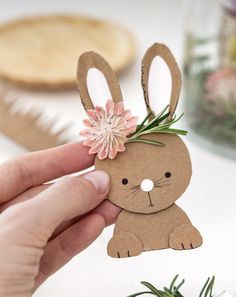 a person holding up a paper bunny with flowers on it's head and the other hand