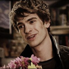 a young man holding a bunch of flowers in his hand and smiling at the camera