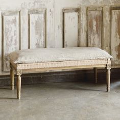 an old wooden bench sitting in front of a white wall with peeling paint on it