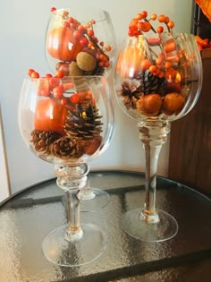 two wine glasses filled with pine cones and oranges on top of a black table