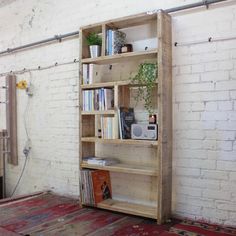 a wooden shelf with books and plants on it in front of a white brick wall