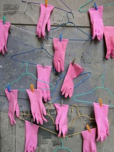 several pairs of pink gloves hanging from clothes pins on a gray wall with blue string