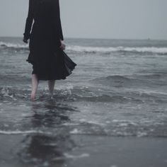 a woman standing in the ocean with an umbrella