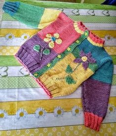 a colorful knitted sweater laying on top of a quilted tablecloth covered in flowers