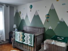 a baby's room with mountains and hot air balloons painted on the wall, along with a crib